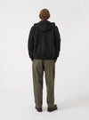 Side view of a model wearing the Black Brush Back Sweat Core Hoody against a neutral studio backdrop. The image shows the side profile of the black sweatshirt, demonstrating the cozy fleece construction, hood structure, and fit.