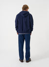 Angled view of a model wearing the Navy Brush Back Sweat Core Hoody against a plain studio background. The image showcases the deep navy hue, comfortable fleece fabric, sleeve cuffs, and overall relaxed silhouette from the side.