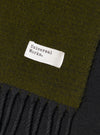 Detailed view of the Green/Black Double Sided Scarf draped flat against a plain studio backdrop. The shot showcases the contrast between the green and black sides, accentuating the soft texture and fringed trim along the edge.