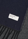 Stylized view of the Navy/Mid Grey Double Sided Scarf arranged flat on a light studio backdrop. The shot showcases the contrast between the dark navy and medium grey tones, emphasizing the soft knit fabric and neat edge fringe.