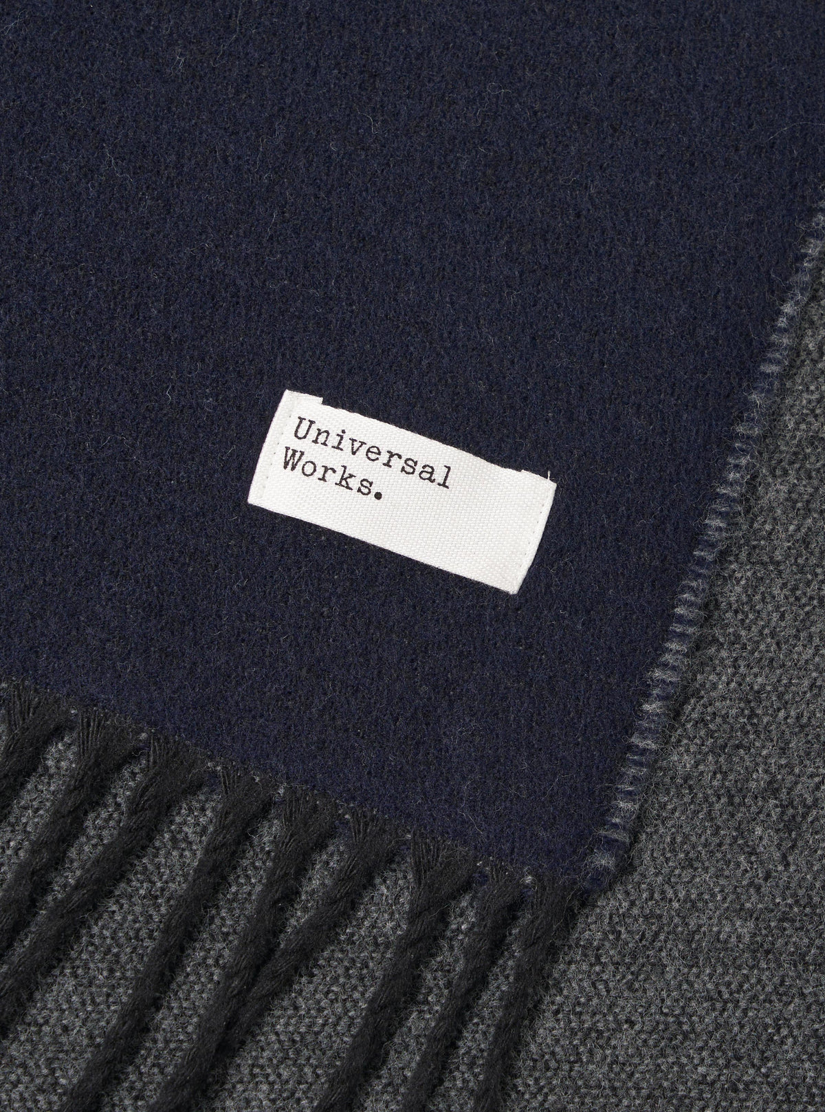 Stylized view of the Navy/Mid Grey Double Sided Scarf arranged flat on a light studio backdrop. The shot showcases the contrast between the dark navy and medium grey tones, emphasizing the soft knit fabric and neat edge fringe.