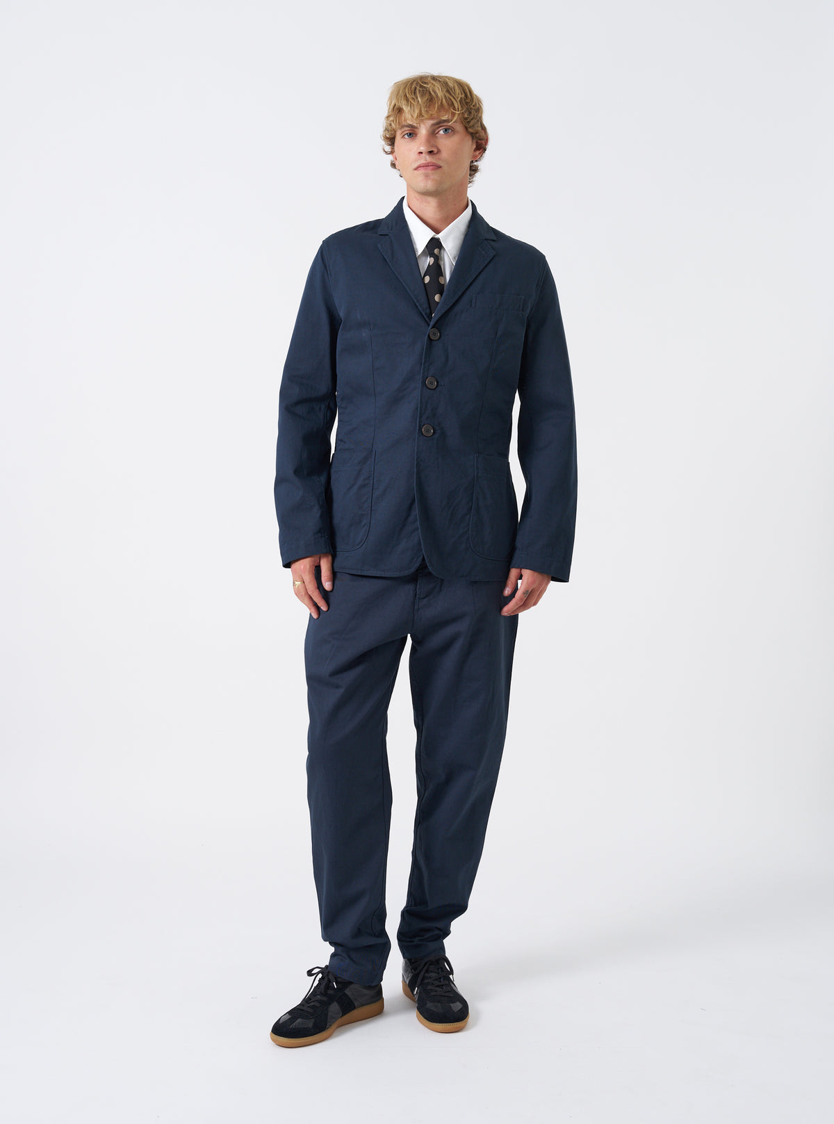Front view of a male model wearing the Navy Twill London Jacket standing against a neutral studio backdrop, showing how the jacket fits across the shoulders and chest in a full styled outfit look.