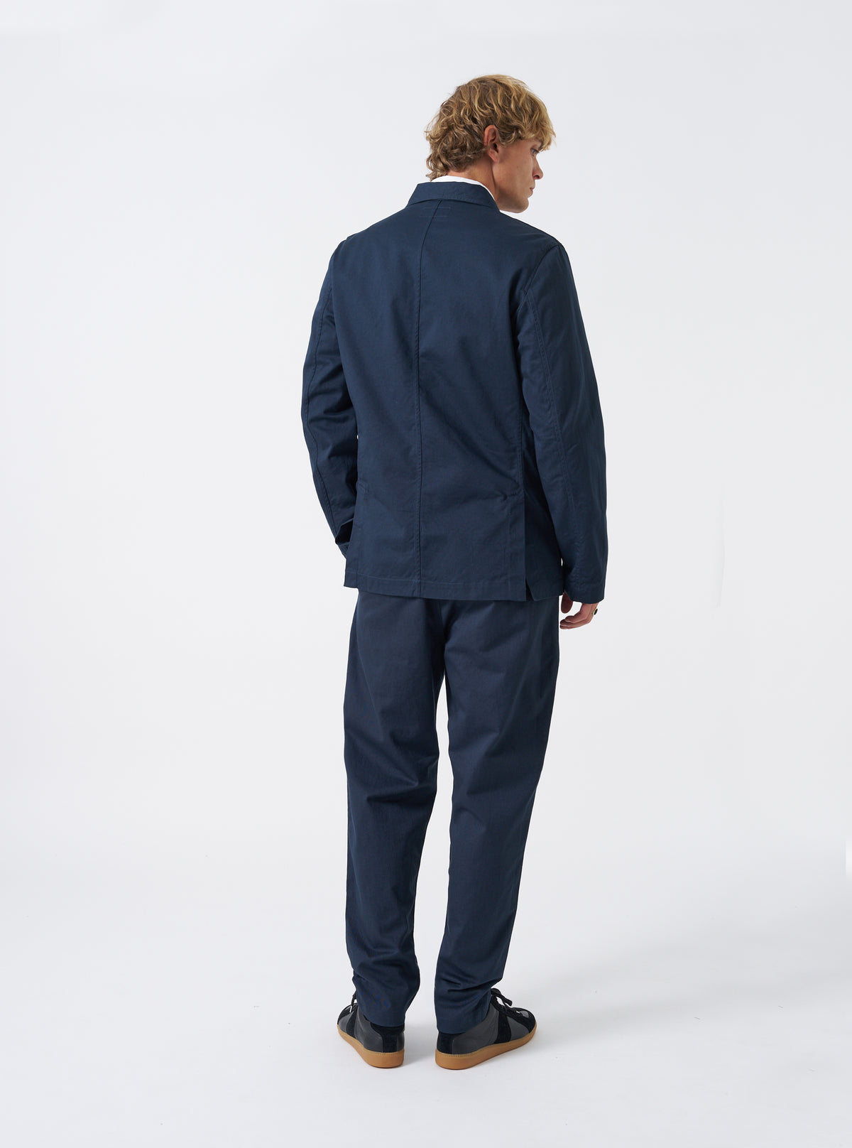 Three-quarter view of a male model wearing the Navy Twill London Jacket in a bright studio environment, demonstrating the jacket drape, arm length, and deep navy blue color against a plain backdrop.