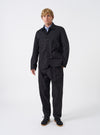 Front view of a male model wearing the Black Twill Bakers Chore Jacket in a minimalist studio setting, layered over a casual shirt to demonstrate the overall regular fit, length, and functional style.