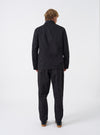 Side view of a male model wearing the Black Twill Bakers Chore Jacket against a neutral backdrop, demonstrating the profile silhouette, sleeve width, shoulder fit, and natural drape of the black twill coat.
