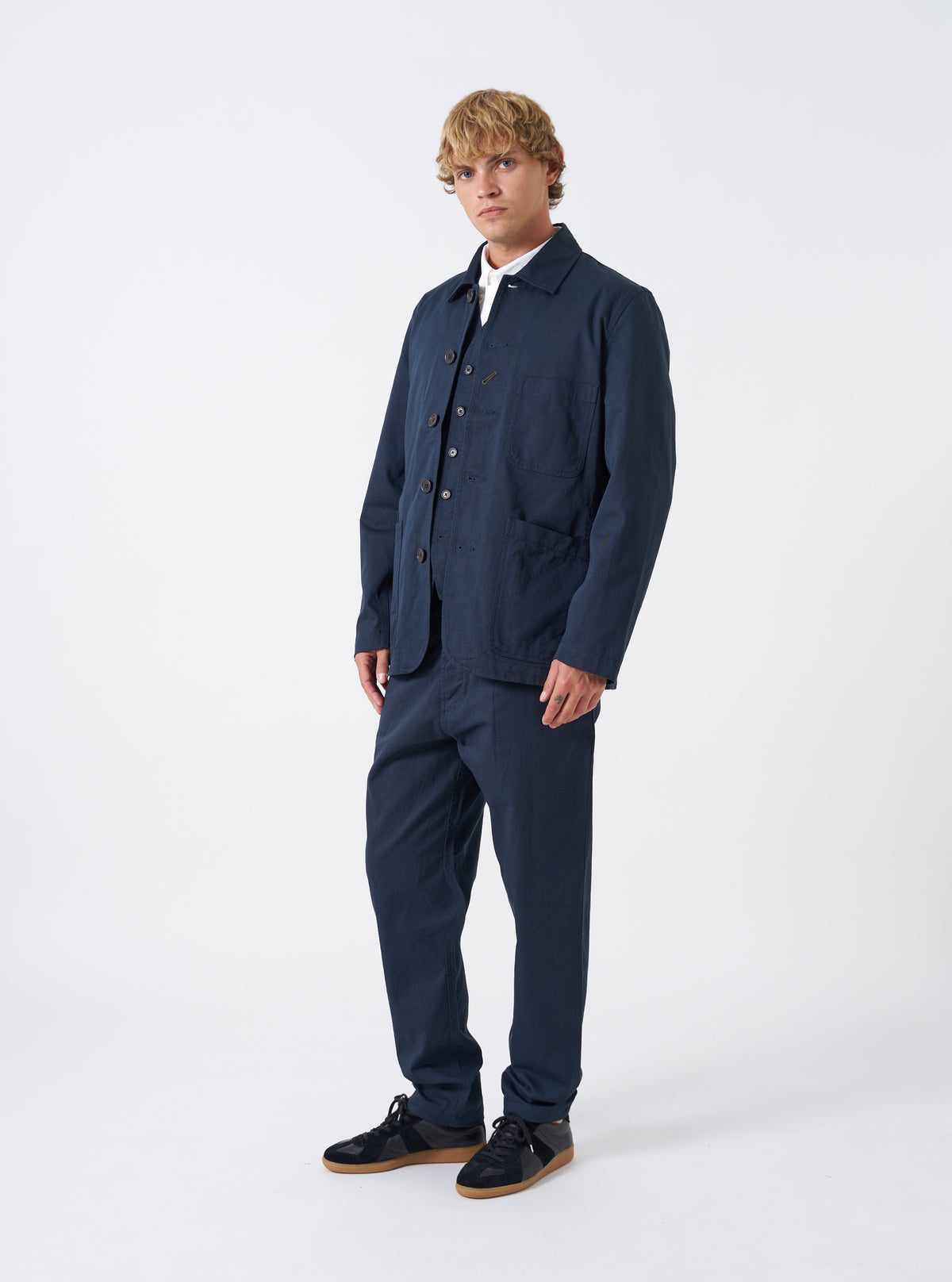 Front view of a model wearing the Navy Twill Bakers Chore Jacket layered over a shirt in a light studio setting. The model stands facing forward, showing the relaxed fit and pocket layout of the navy jacket.