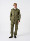 Front view of a model wearing the Light Olive Twill Bakers Chore Jacket in a bright studio setting. The model stands facing forward, showing the front button closure, collar, and utility pockets in light olive green.