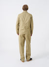 Rear view of a model wearing the Sand Twill Bakers Chore Jacket in a light studio background. The model stands facing away, displaying the drape, fit across the back, and overall silhouette.