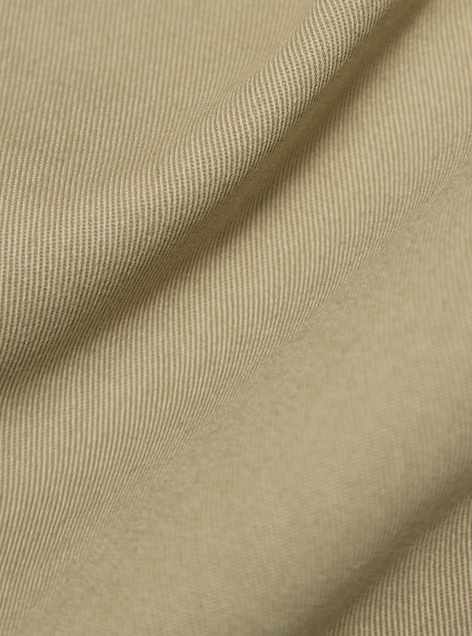 Close-up of the sand-colored twill fabric of the Sand Twill Bakers Jacket, showing texture and drape. Studio shot.