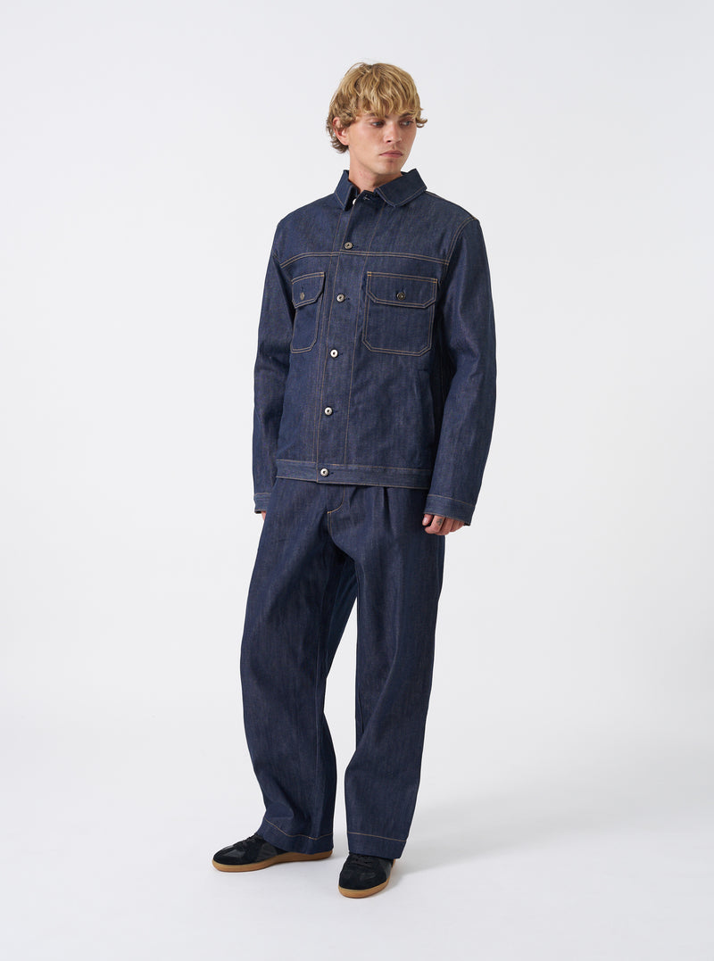 Front view of the Indigo 13oz Selvedge Denim Trucker Jacket displayed against a clean white background. The deep blue jacket features classic stitch details, dual chest pockets, and silver button closures along the front placket.