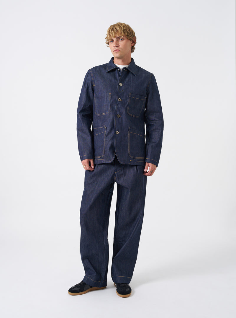 Full front shot of the Indigo 13oz Selvedge Denim Bakers Chore Jacket laid flat against a clean off-white background, highlighting button closures, patch pockets, and rich blue finish.