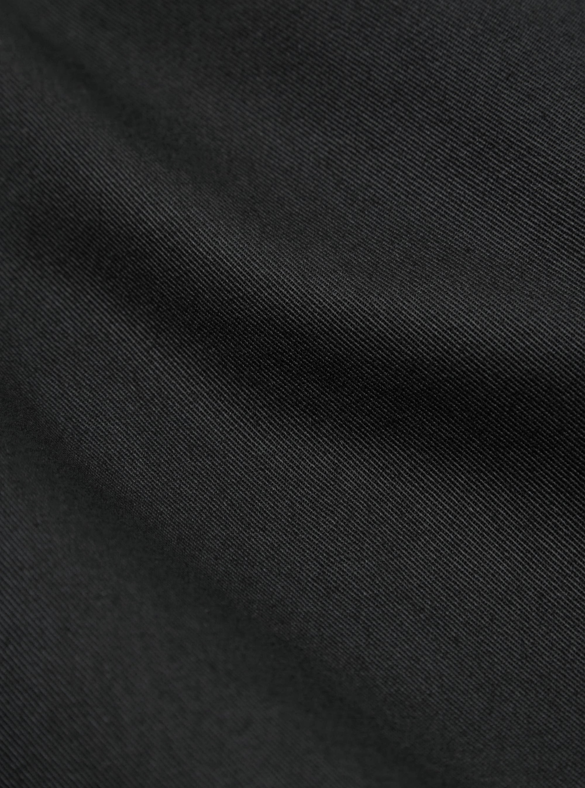 Close-up of the Black Twill Curved Pant, showing the fabric's texture and drape. The twill weave is visible, creating a subtle pattern. 
