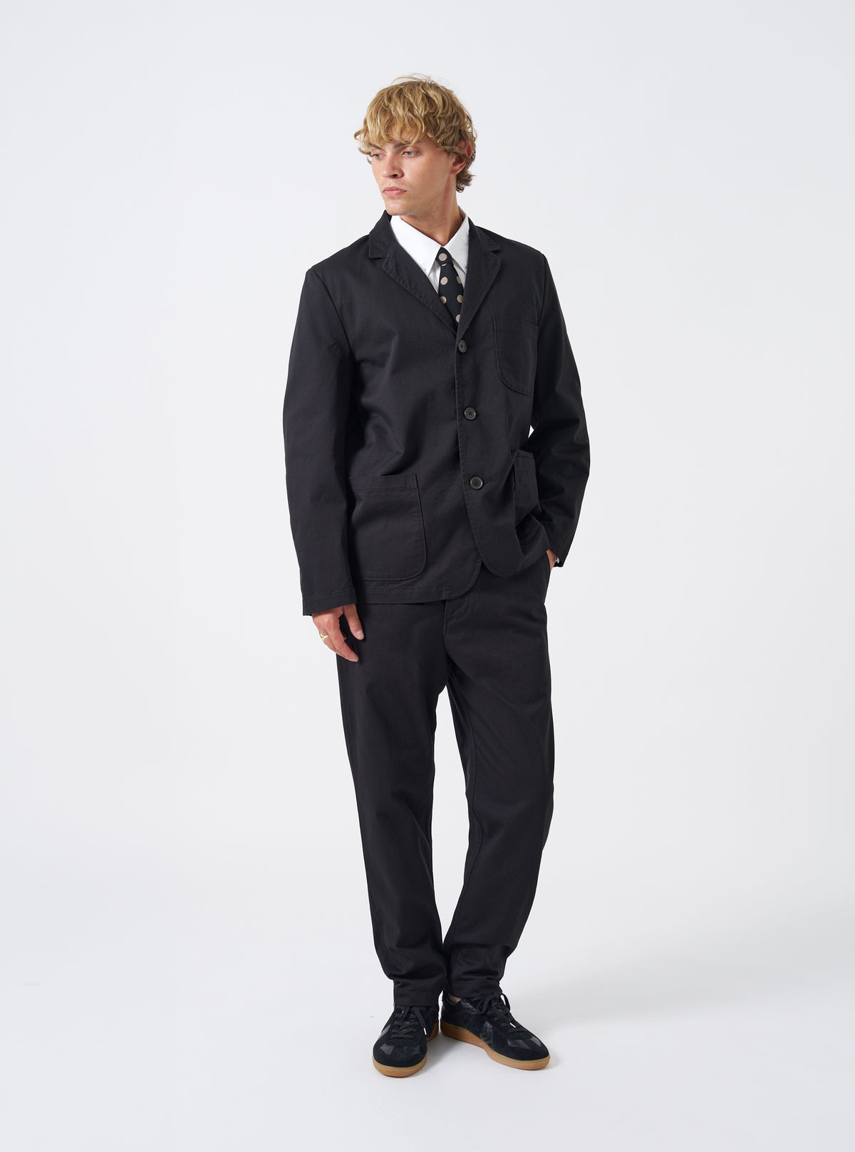 A model wearing the Black Twill Three Button Jacket indoors against a minimalist neutral backdrop, styled with the front buttons fastened, showcasing a tailored fit and structured shoulders.