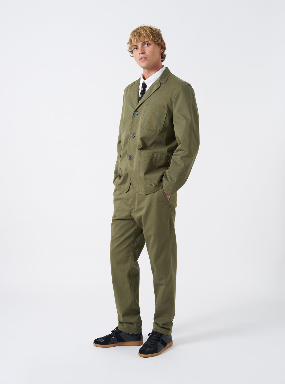 A model wearing the Light Olive Twill Three Button Jacket standing against a plain backdrop, featuring a front-facing view that highlights the tailored fit and olive green tone.