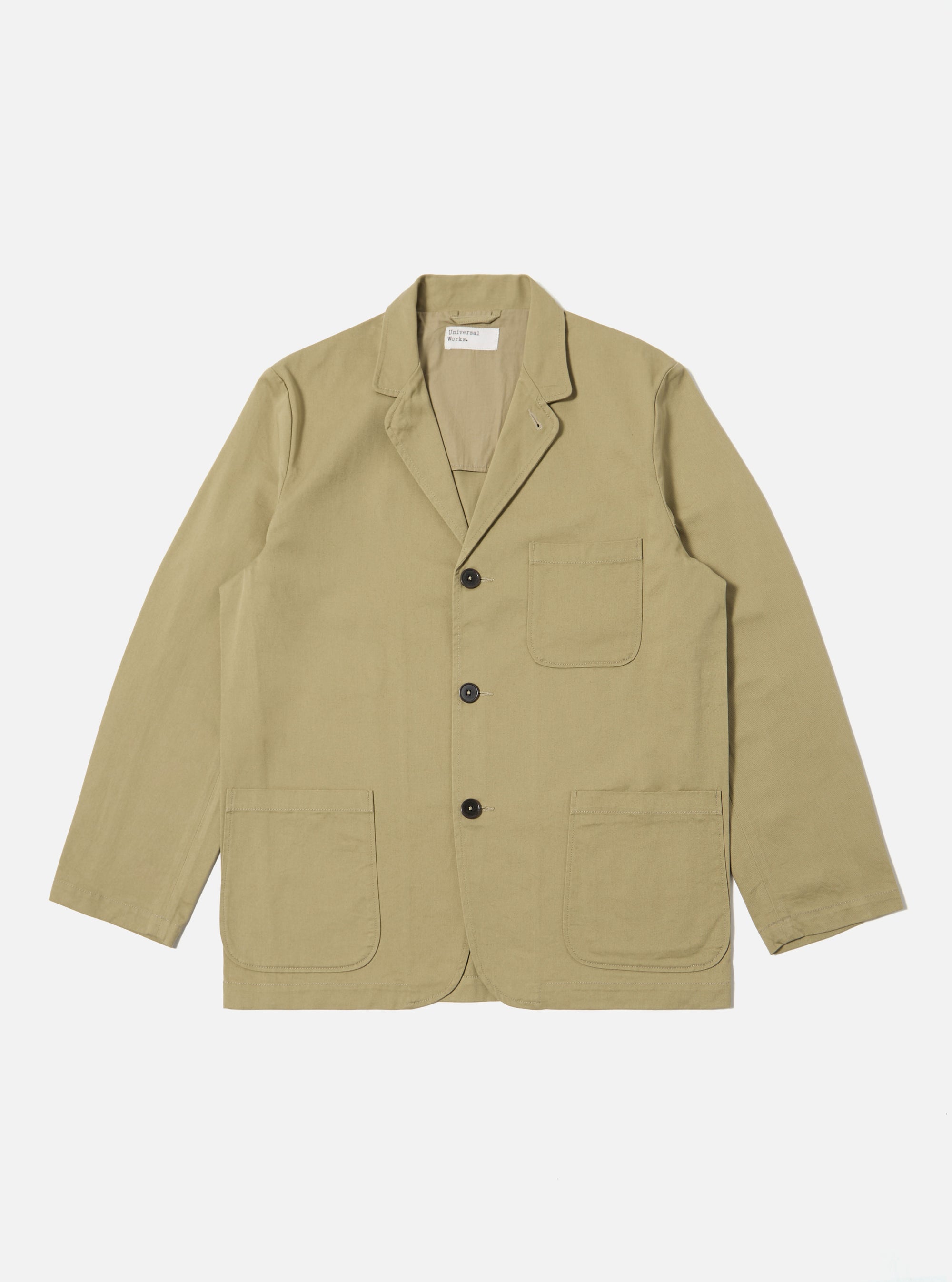 The Sand Twill Three Button Jacket is laid flat on a white background. The jacket is a light tan color and made of twill. It has three dark buttons and two large pockets.