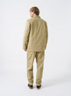 Side profile view of a male model wearing the Sand Twill Three Button Jacket against a clean studio background. Demonstrates the natural shoulder line, tailored sleeve cut, and relaxed silhouette.