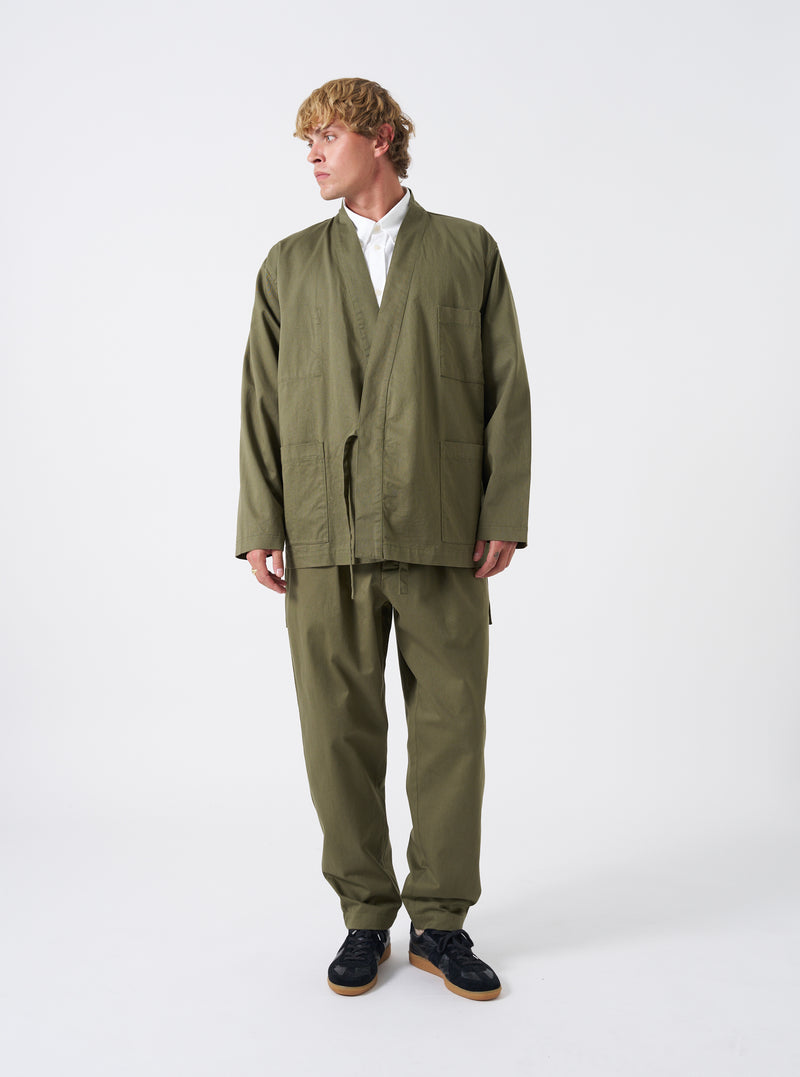 A male model is wearing the Light Olive Twill Kyoto Work Jacket, shown from a three-quarter angle against a white studio background. The jacket is styled open to reveal the layered outfit.