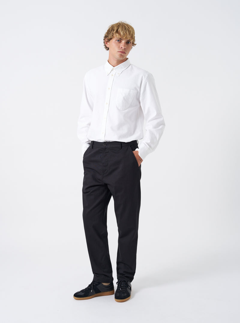 Full front shot of a model wearing the Black Twill Military Chino on a clean white background. The model wears the black trousers paired with casual shoes, demonstrating the comfortable mid-rise fit and neat taper toward the ankles.
