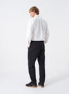 Rear view of a model wearing the Black Twill Military Chino against a plain white studio backdrop. Highlights how the dark cotton twill trousers fit through the seat and thighs, featuring rear jetted button pockets and clean hem finish.
