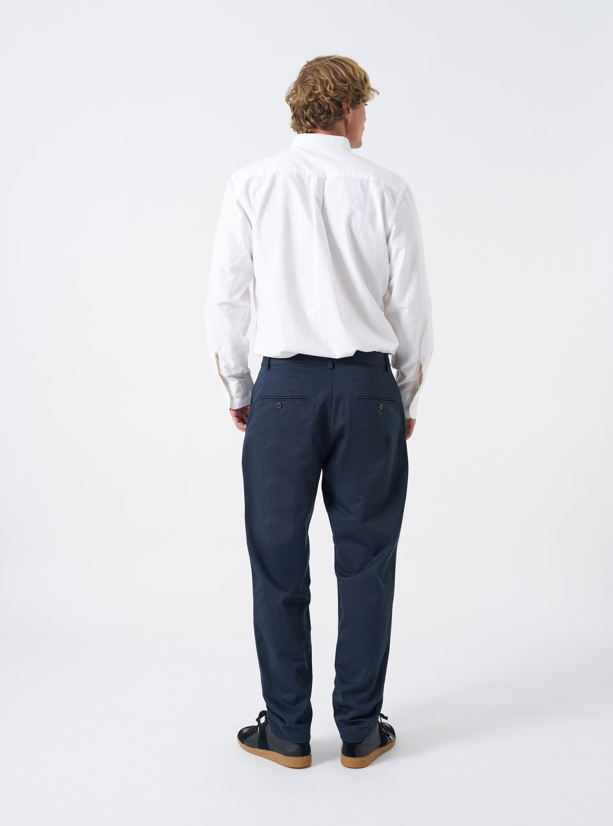 Back view of a model wearing the Navy Twill Military Chino against a white background. Demonstrates the fit around the waist and seat, showing the rear jetted button pockets and straight-to-tapered cut on the navy cotton trousers.
