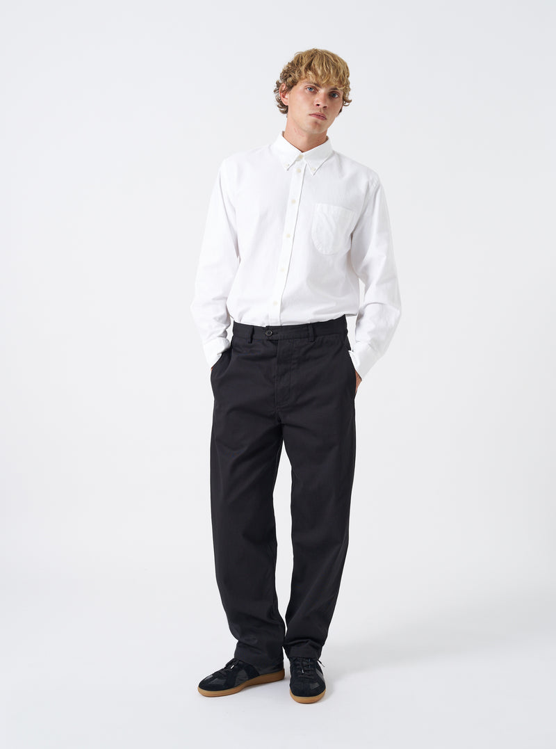 Full-length front shot of a model wearing the Black Twill Curved Pant against a plain off-white studio backdrop. The model wears the trousers paired with shoes, showcasing the loose curved leg shape and dark twill drape.