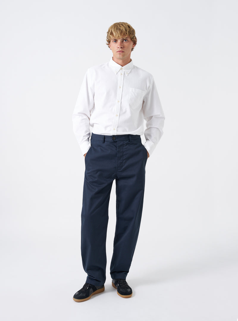 Full front perspective of a model wearing the Navy Twill Curved Pant on a clean off-white background. The model displays the rich navy trousers paired with casual shoes, showing the curved leg cut and flat front waistband.