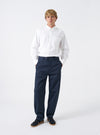 Full front perspective of a model wearing the Navy Twill Curved Pant on a clean off-white background. The model displays the rich navy trousers paired with casual shoes, showing the curved leg cut and flat front waistband.
