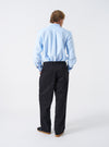 Back view shot of a model wearing the Navy Twill Duke Pant against a clean neutral studio backdrop. The model stands wearing the dark navy pants, demonstrating the relaxed drape, back patch pockets, and slight leg taper.