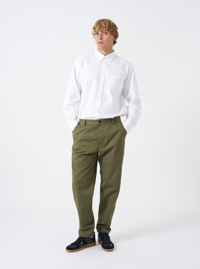 Front full-length view of a male model wearing the Light Olive Twill Aston Pant on a neutral studio background. Displays the slim straight fit, low rise waist, angled hand pockets, and natural drape of the light olive green twill trousers.