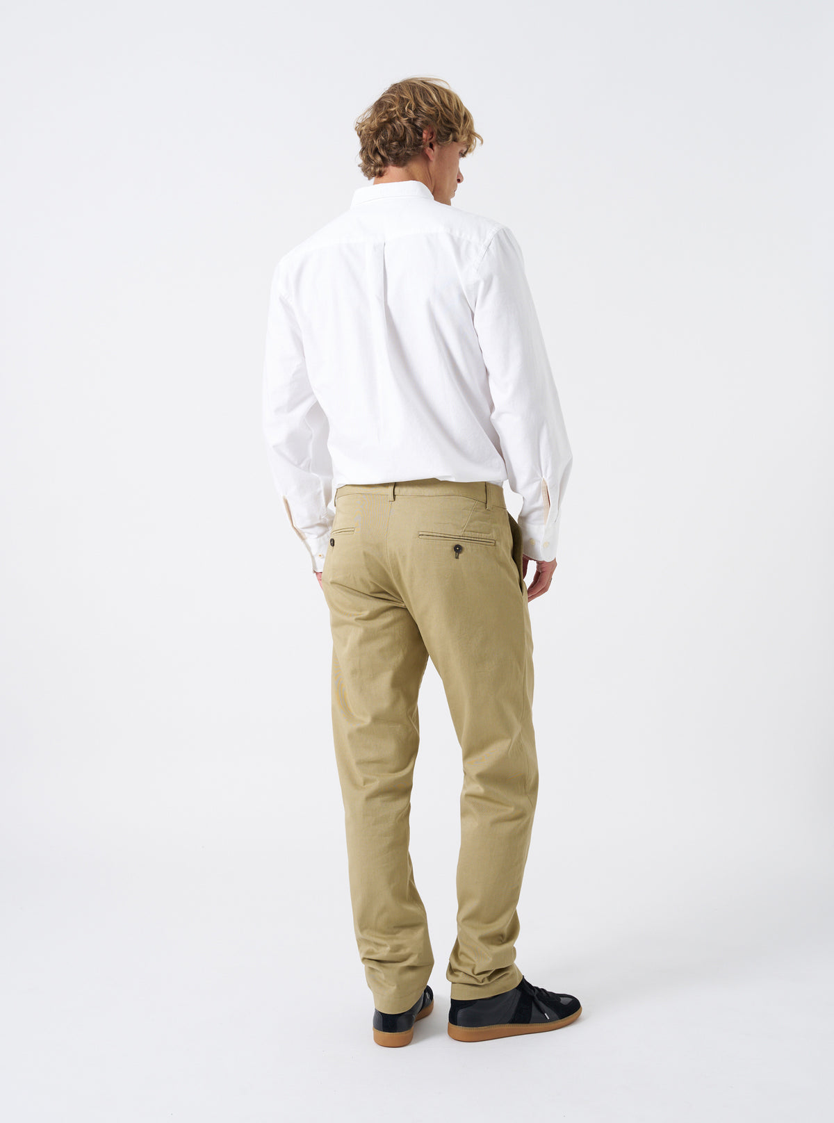 Side and rear angle view of a male model wearing the Sand Twill Aston Pant against a plain studio background. Demonstrates the clean straight-leg profile, low-rise waist fit, and rear pocket placement on the sand twill trousers.