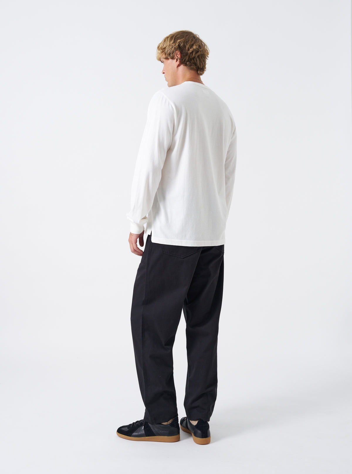 Rear view of a male model wearing the Black Twill Fatigue Pant set against a plain studio backdrop. Shows the fit across the seat, rear buttoned patch pockets, waist adjustment tabs, and straight-leg drop in black cotton twill.