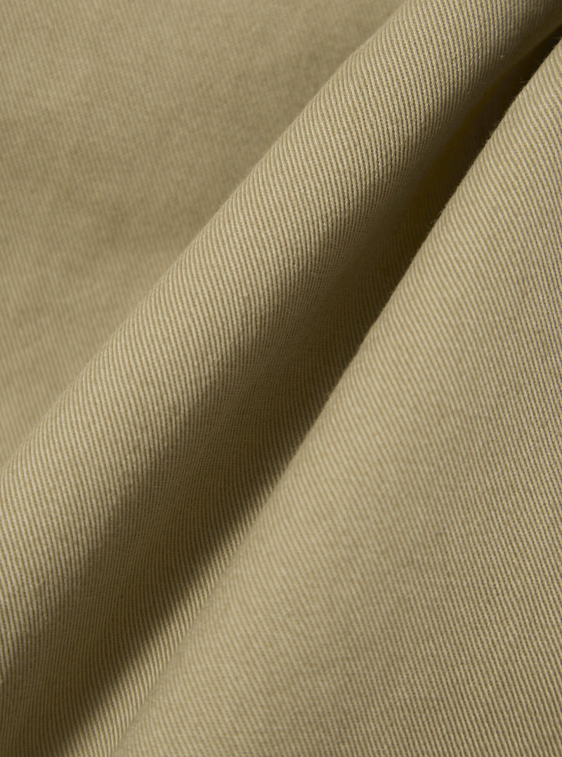 Close-up of the Sand Twill Fatigue Pant fabric. The material is a light tan color with a visible twill weave. The fabric is draped to show texture.