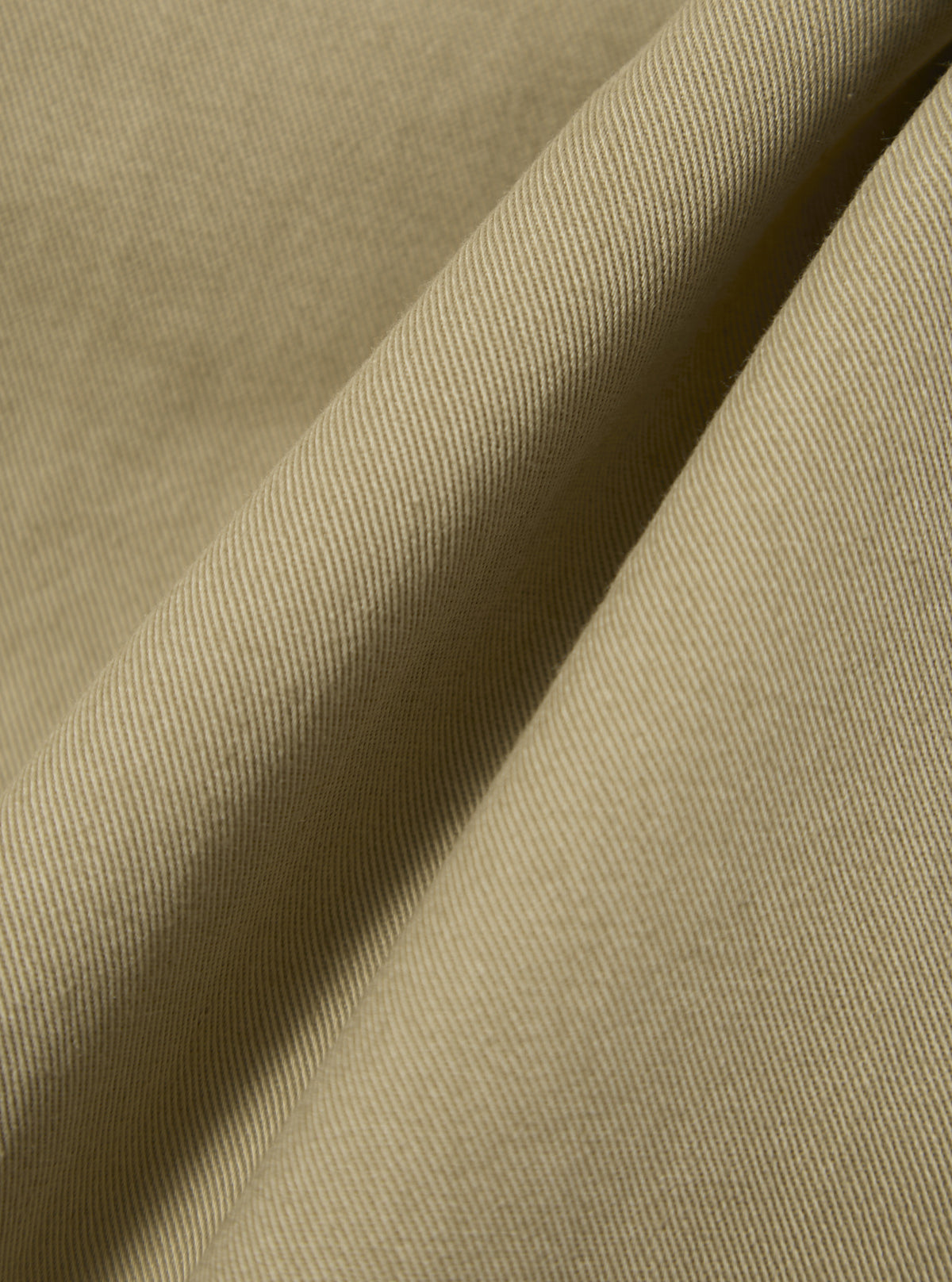 Close-up of the Sand Twill Fatigue Pant fabric. The material is a light tan color with a visible twill weave. The fabric is draped to show texture.