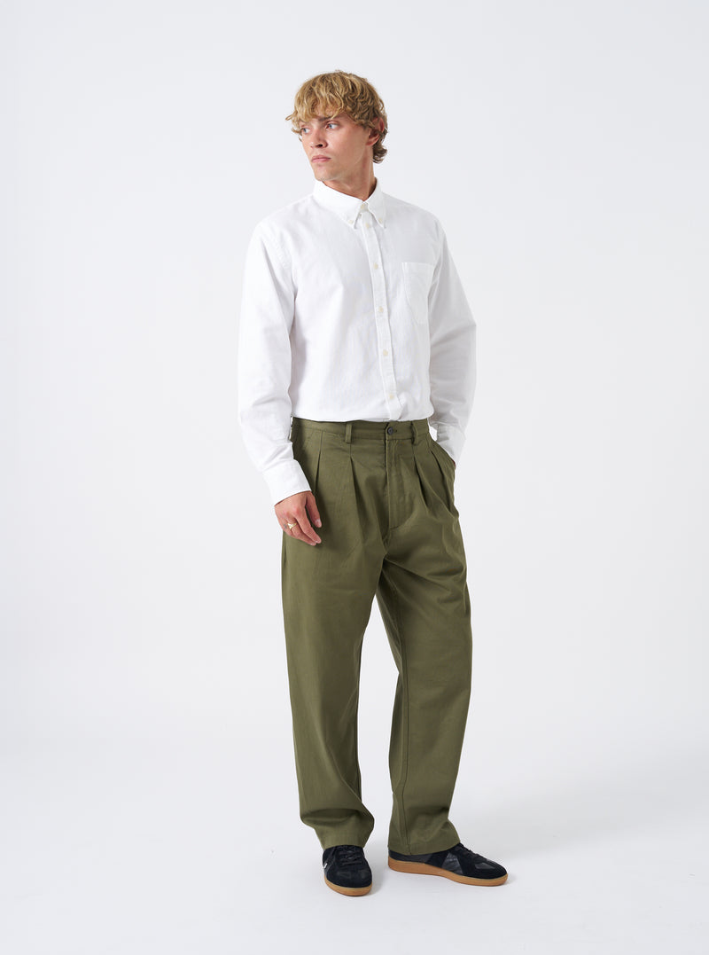 Full-length shot of a model wearing the Light Olive Twill Double Pleat Pant paired with shoes on a plain studio background. Showcases the relaxed wide leg fit, front double pleats, side pockets, and light olive color.