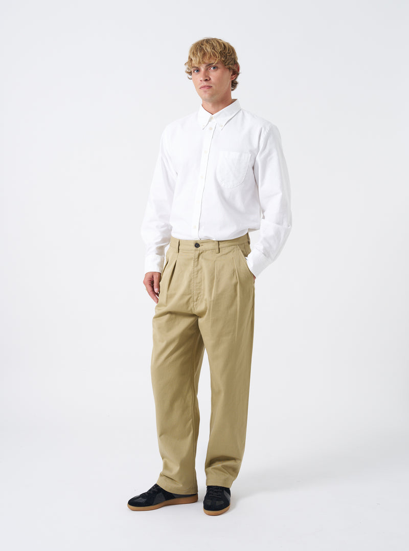 Full-length studio shot of a model wearing the Sand Twill Double Pleat Pant on a plain backdrop. Highlights the loose wide-leg silhouette, front pleats, and sand colorway styled with footwear.