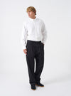 A full-length front view of a model wearing the Black Twill Double Pleat Pant against a plain studio background. Shows how the wide-fit pleated trousers drape comfortably over footwear on the model.