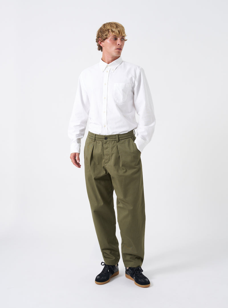 Full-length shot of a model wearing the Light Olive Twill Pleated Track Pant against a neutral background. Shows the relaxed tapered leg fit, drawstring waist, and soft drape of the twill fabric.