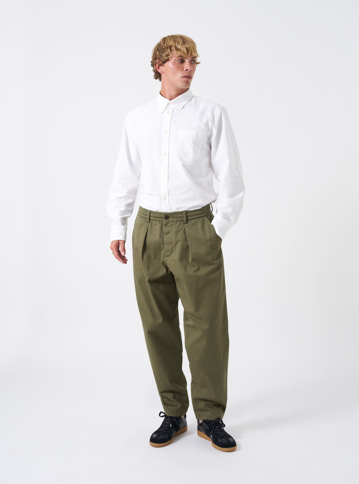 Full-length shot of a model wearing the Light Olive Twill Pleated Track Pant against a neutral background. Shows the relaxed tapered leg fit, drawstring waist, and soft drape of the twill fabric.