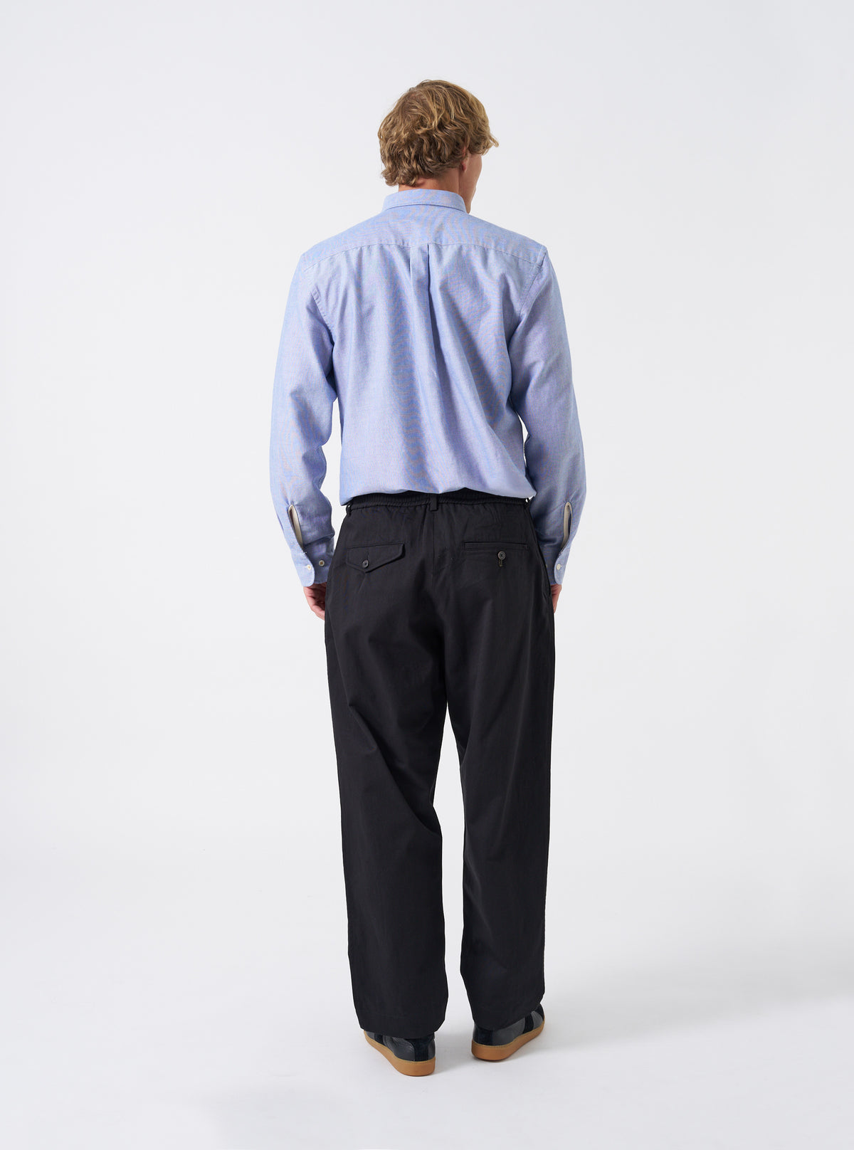 Additional shot of a model wearing the Black Twill Pleated Track Pant on a neutral background. Highlights the movement and drape of the pleated black twill fabric along with the casual tapered fit.