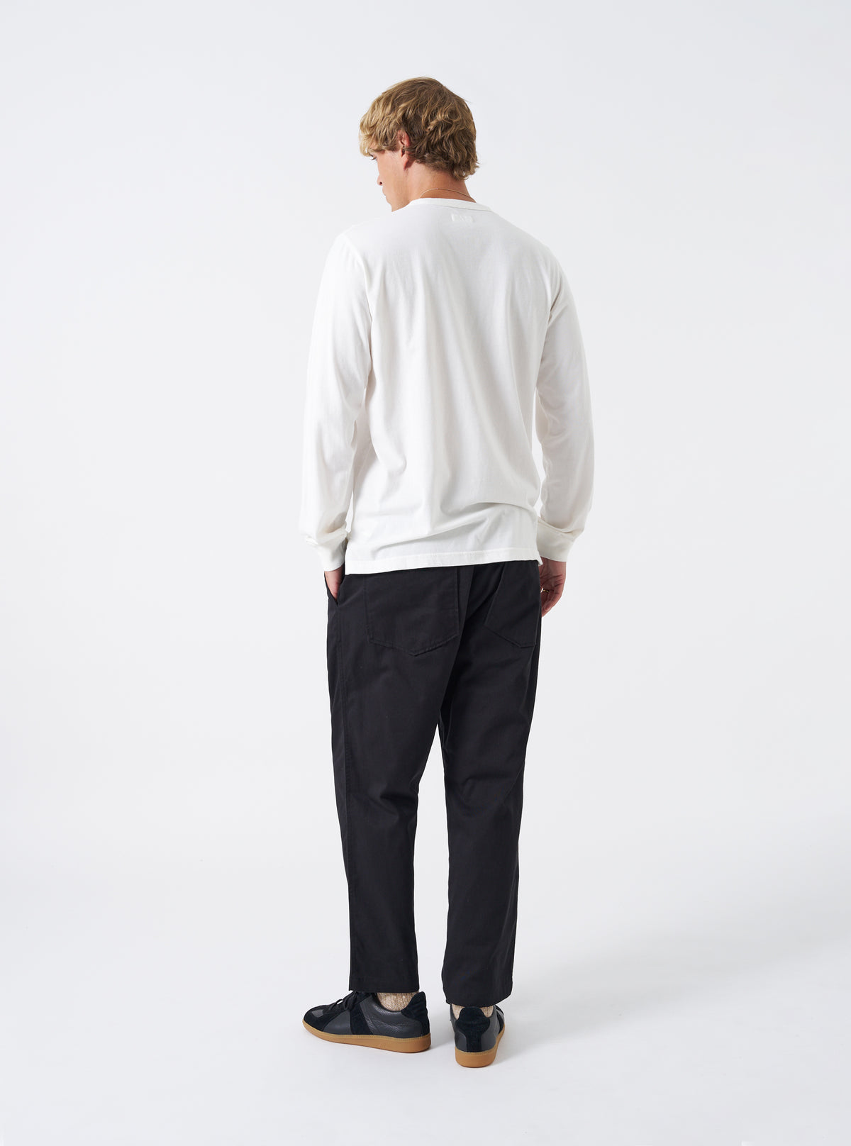 A model wears the Black Twill Hi Water Trouser set against a clean white background. The rear perspective showcases the back patch pockets, comfortable elasticated waistband, relaxed fit, and cropped hem above the ankles.