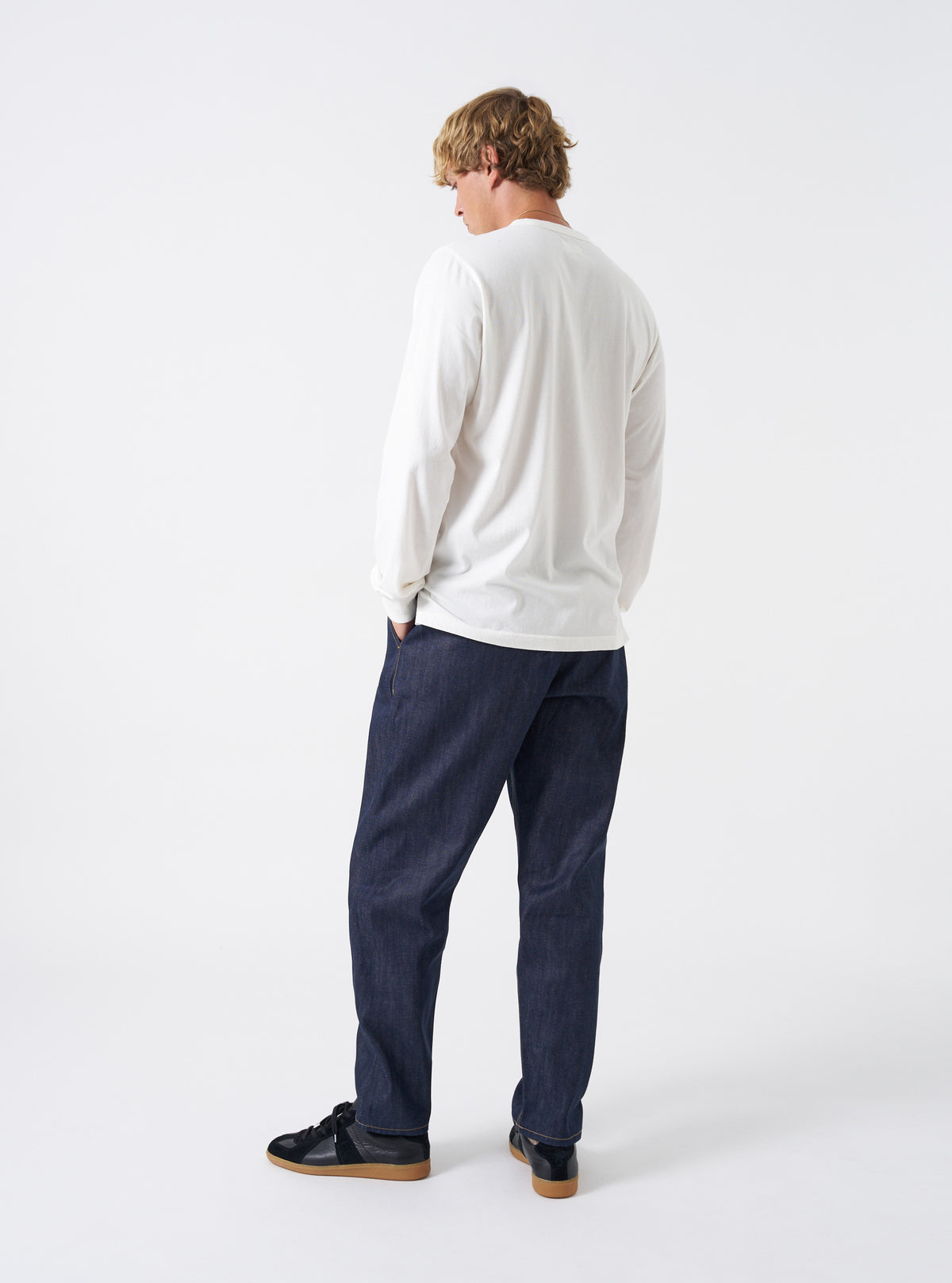 Back perspective of the Indigo 13oz Selvedge Denim Military Chino on a clean white background. Highlights two rear welt pockets, structured seat construction, contrast seam stitching, and the tapered hem line of the denim pants.