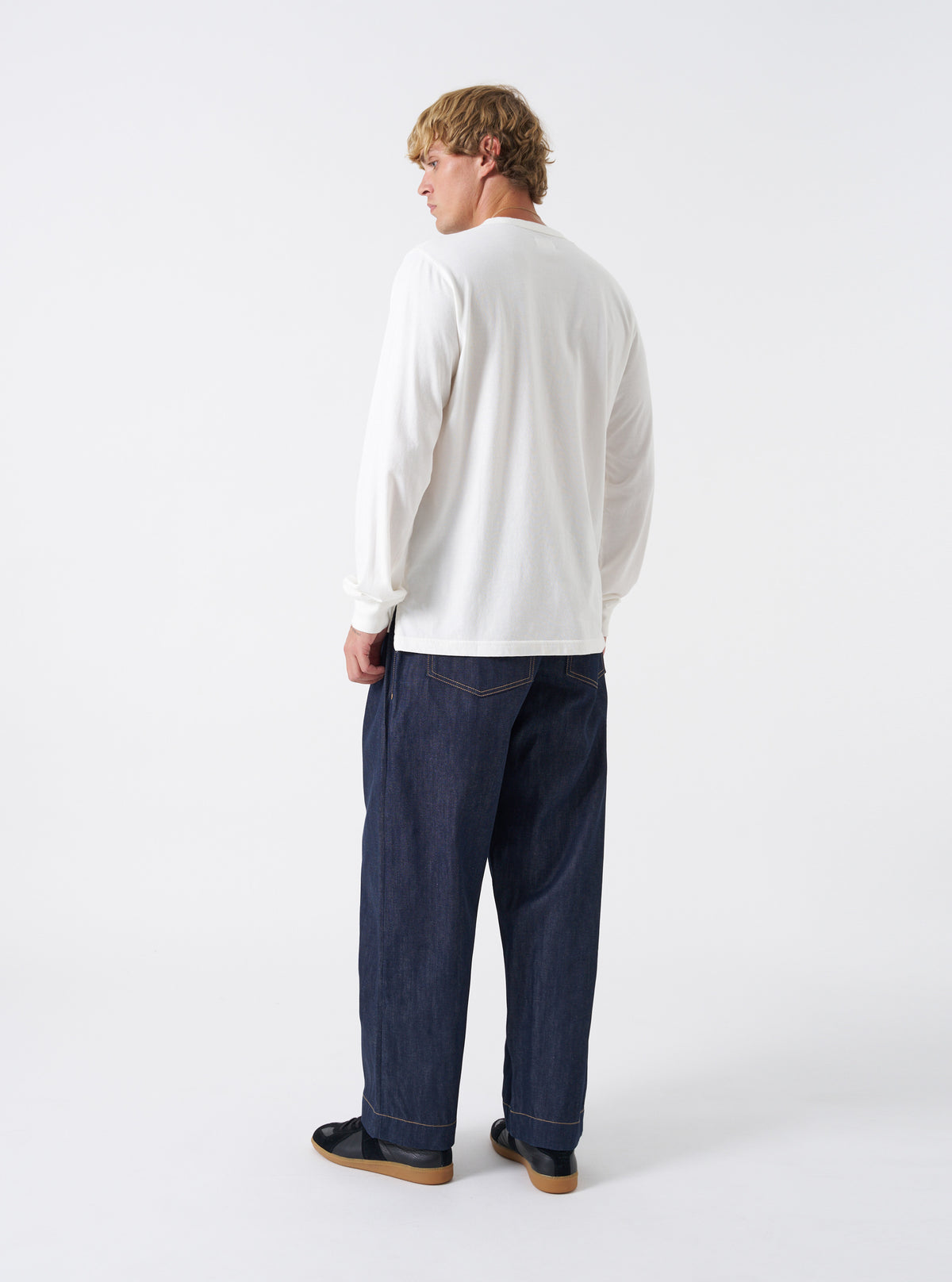 Rear view of the Indigo 13oz Selvedge Denim Duke Pant shown against a plain white studio backdrop. Features two spacious back patch pockets, clean waistband stitching, structured back yoke, and wide tapered legs.