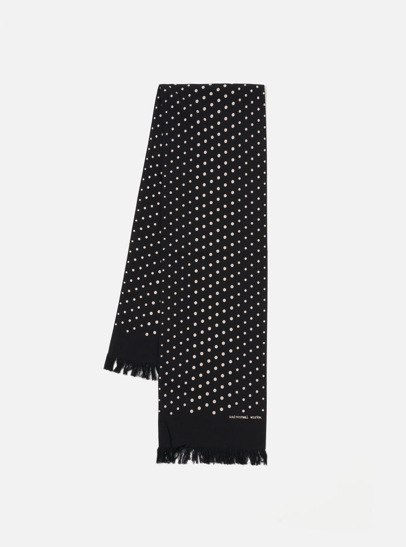 Draped on a white surface, a Black Dot Print Short Scarf. The black scarf features small white dots and a fringed edge. The brand name is printed near the bottom.