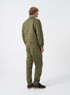 A model wears the Light Olive Twill MW Fatigue Jacket turned to show the side and back profile against a plain studio backdrop. The shot highlights the comfortable shoulder fit, sleeve cuffs, and hip-length hemline.