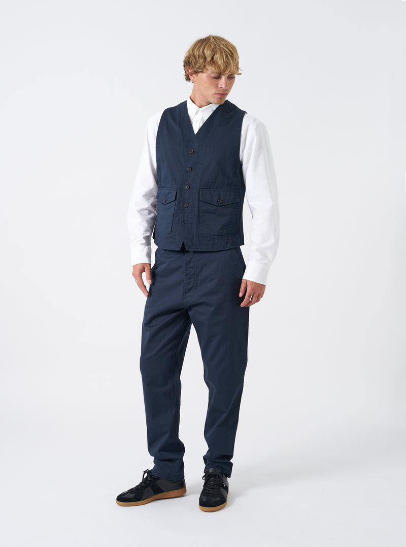 A model stands against a plain studio background wearing the Navy Twill Field Waistcoat over a shirt. The front view shot highlights the tailored layer fit, V-neck front, multiple patch utility pockets, and dark navy twill cotton fabric texture.