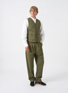 A model stands against a plain studio backdrop wearing the Light Olive Twill Field Waistcoat over a collared shirt. The shot displays the relaxed fit, front button closure, distinct olive twill fabric shade, and front utility patch pockets.