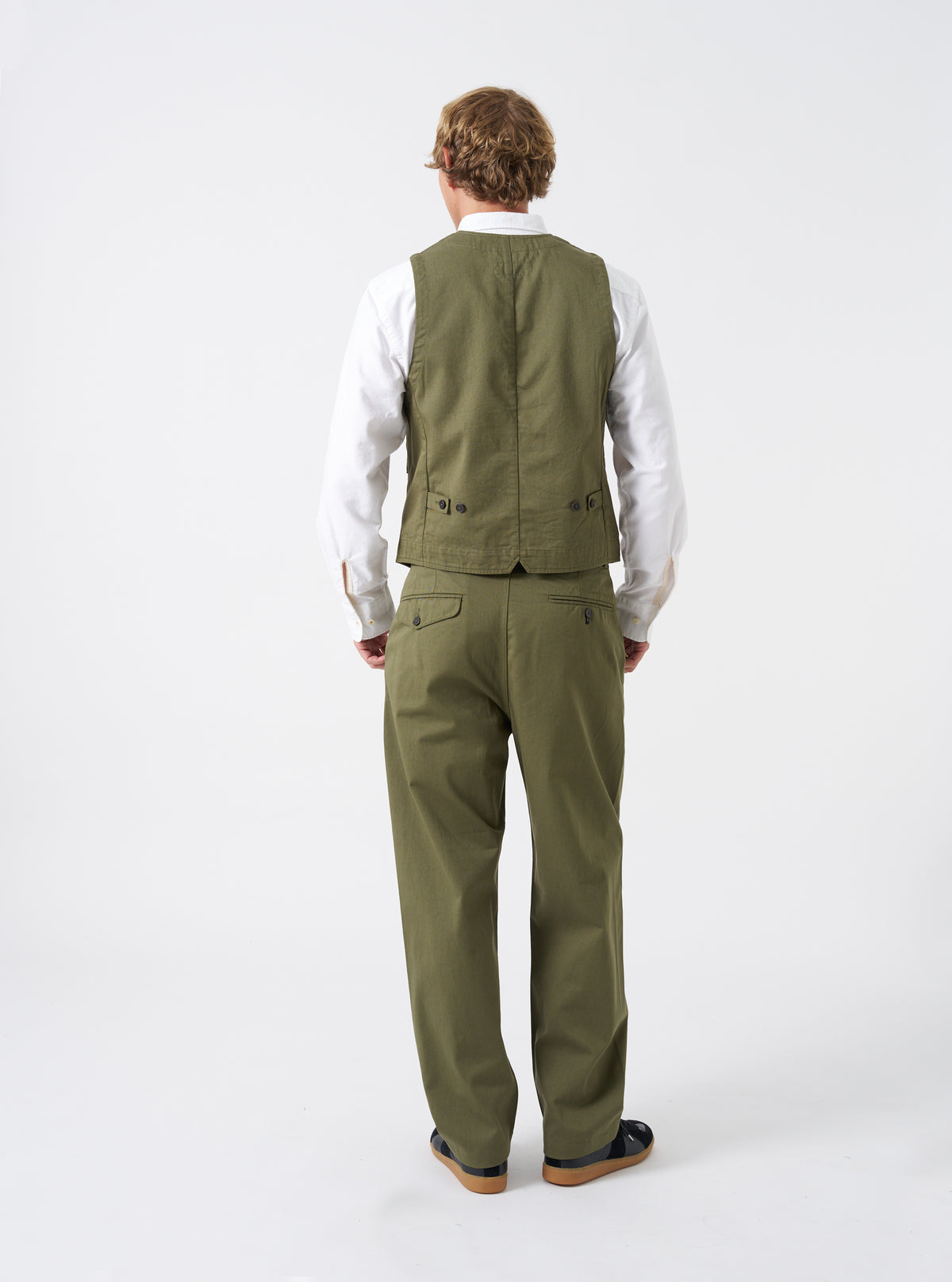 A model wears the Light Olive Twill Field Waistcoat against a clean neutral studio background. The side perspective highlights the structured profile, comfortable layering cut, light olive cotton twill material, and neat pocket stitching.