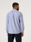 A man stands against a white backdrop, showcasing the back of a Blue Oxford Daybrook Shirt. The shirt is paired with dark trousers. 