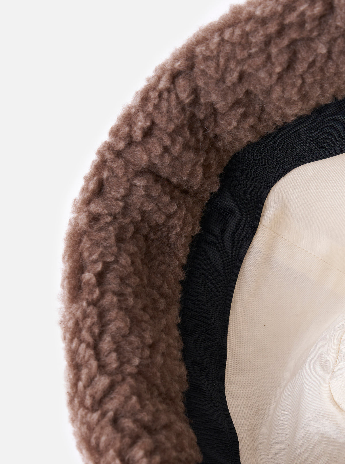 Close-up of the inside of a cableami® Brown Toque Boa Cap. The hat has a brown, boa-like exterior, a black band, and a cream-colored lining. Shot on a white background.