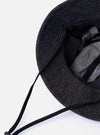 The cableami Black 10oz Denim Metro Hat is shown from a side angle as a flat lay against a plain white background. The image highlights the hat's rounded crown construction and the downward-sloping brim made from black denim with a visible natural slub texture. A black adjustable cord with a toggle is attached to the hat.